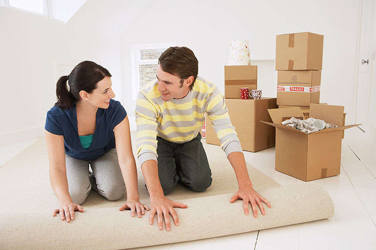 couple unrolling carpet in new home